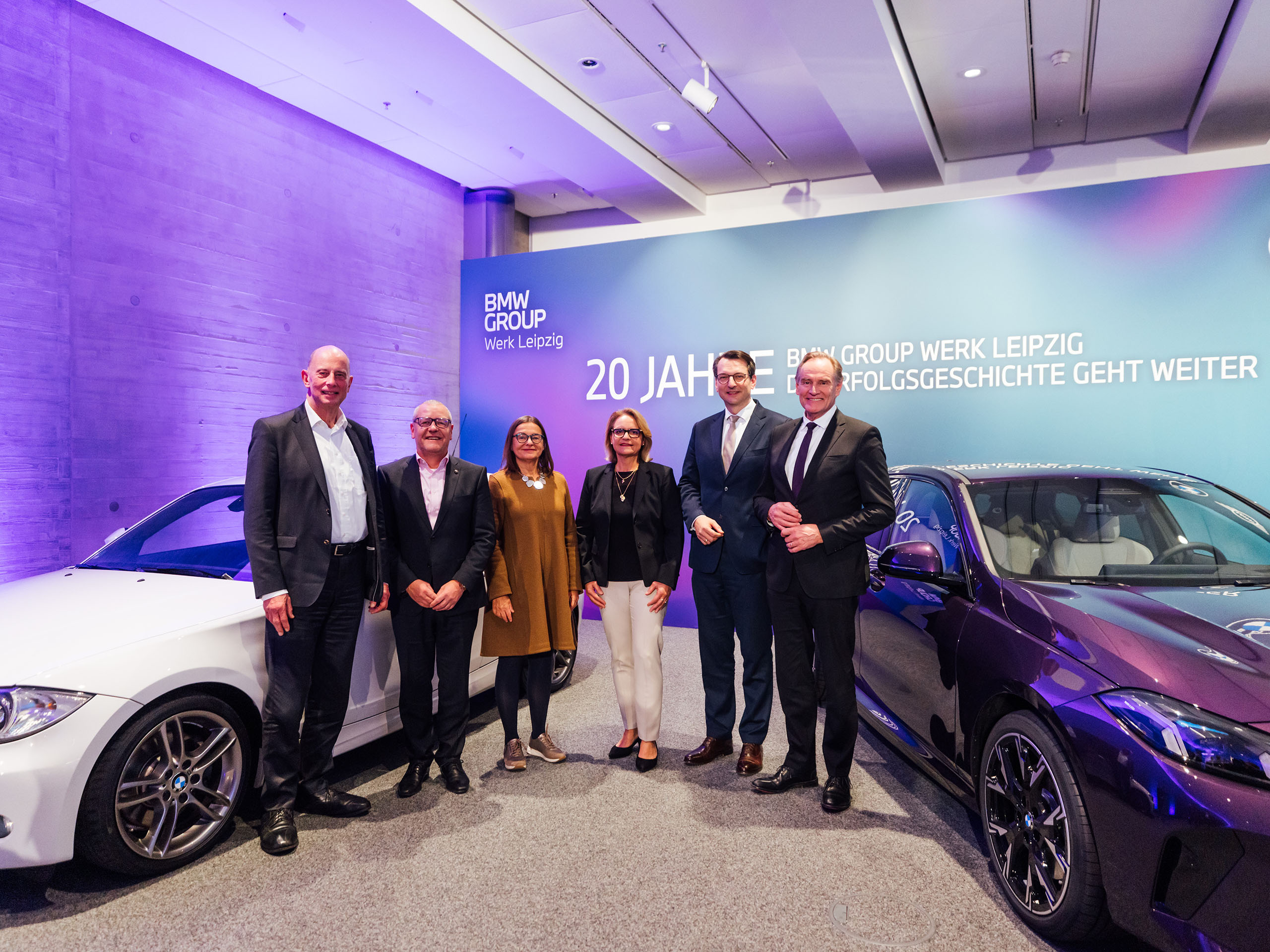 Wolfgang Tiefensee, former Mayor of Leipzig; Jens Köhler, Chairman of the Works Council at BMW Group Plant Leipzig; Barbara Meyer, Saxon State Secretary; Petra Peterhänsel, Head of BMW Group Plant Leipzig; Milan Nedeljković, Member of the Board of Management for Production of BMW AG; and Burkhard Jung, Mayor of Leipzig, standing between a BMW 1 Series (E87) and a BMW 2 Series Gran Coupé (F74).