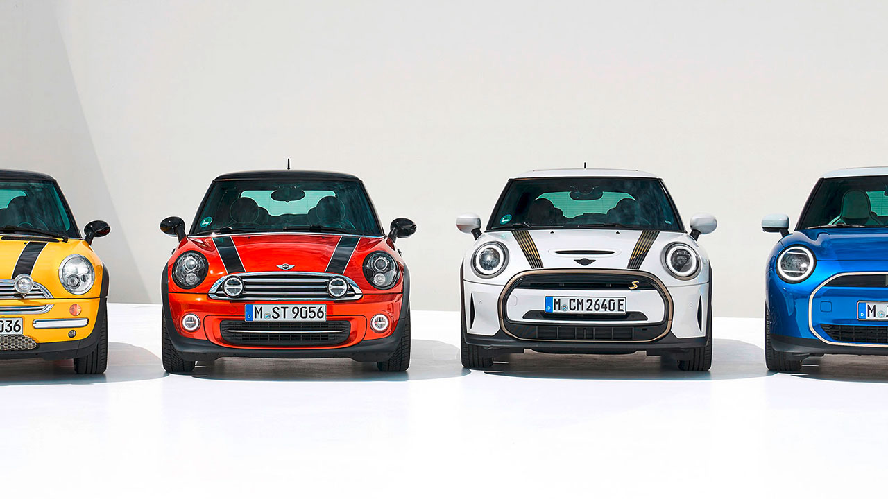 Four generations of MINI Cooper are shown from the front against a white backdrop. From left to right: a yellow second-generation Mk I MINI Cooper, a red third-generation Mk II MINI Cooper, a white fourth-generation Mk II MINI Cooper and a blue MINI Cooper SE.