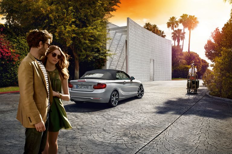 A young couple on holiday standing in front of a BMW 2 Series Convertible.