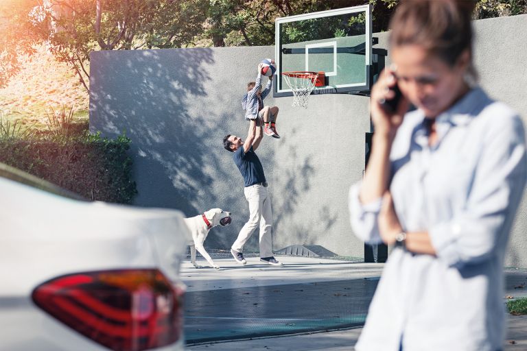 A woman makes a phone call, while the rest of the family plays basketball in the background.