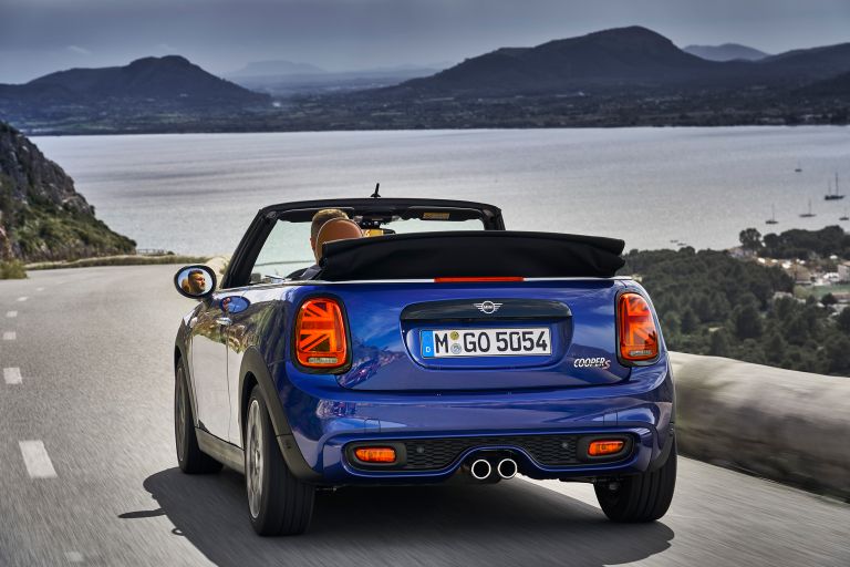 A blue MINI convertible on a road by a lake