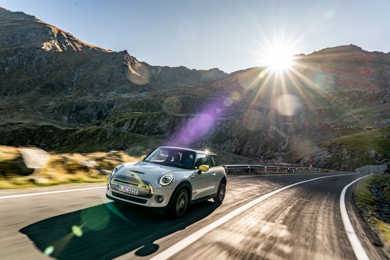 The MINI electric on a mountain road, the sun behind it