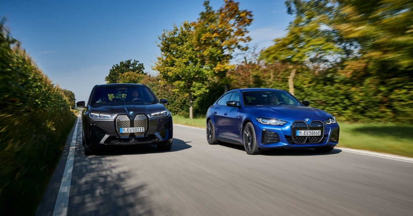 Zwei BMWs fahren nebeneinander auf einer Straße entlang durch eine grüne Umgebung.