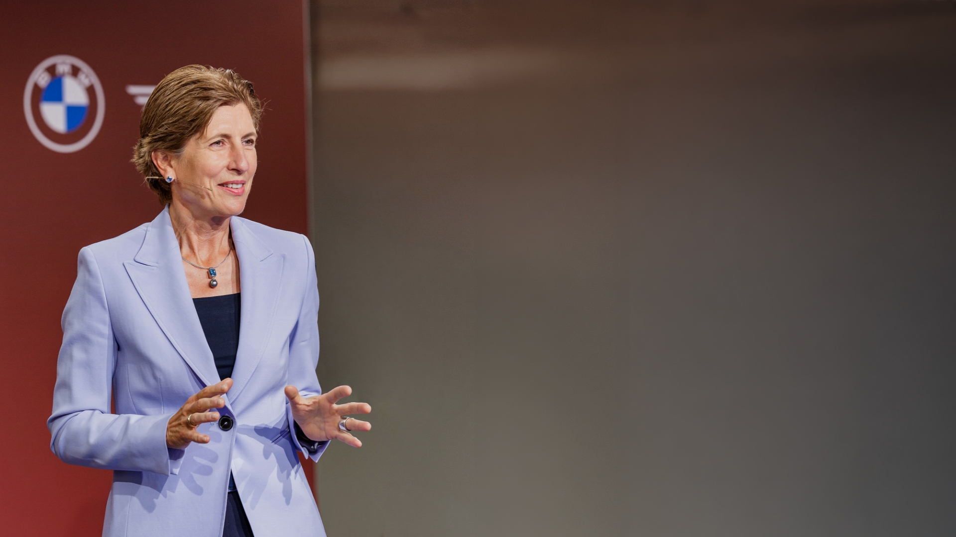 Ilka Horstmeier in hellem Blazer auf B&uuml;hne vor rotem Hintergrund mit BMW‑Logo, mit Headset‑Mikrofon und gestikulierenden H&auml;nden.