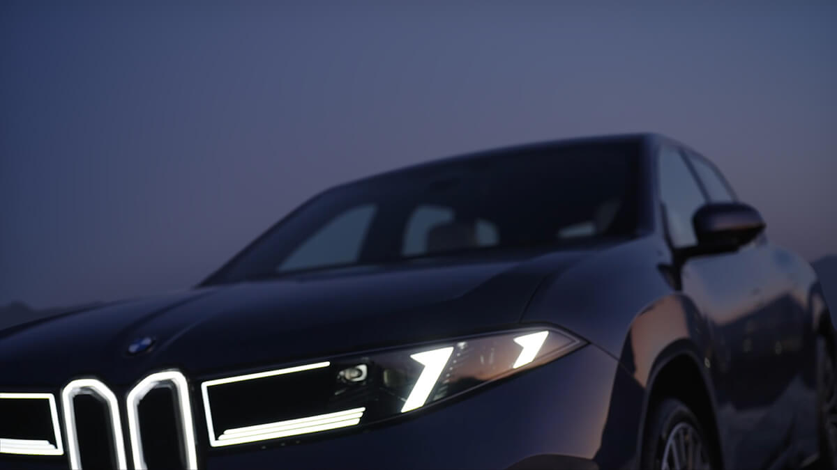 Front eines BMW Fahrzeugs mit leuchtenden LED‑Scheinwerfern und beleuchteter Doppelniere vor dunklem Himmel in der D&auml;mmerung.