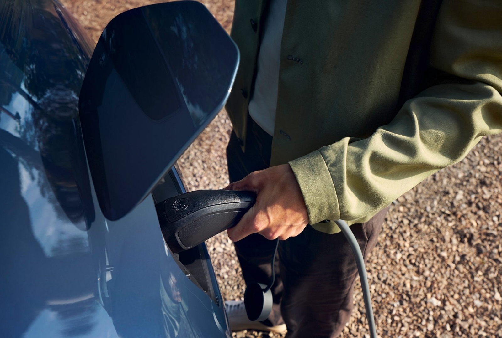 Ein Mann lehnt an einem ladenden BMW, eine Frau steht dahinter. Beide schauen aufs Meer.