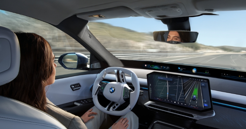 Fahrzeuginnenraum eines BMW mit automatisiertem Fahrmodus, zentralem Display mit Navigationsansicht und entspannt sitzender Person auf der Fahrerseite.
