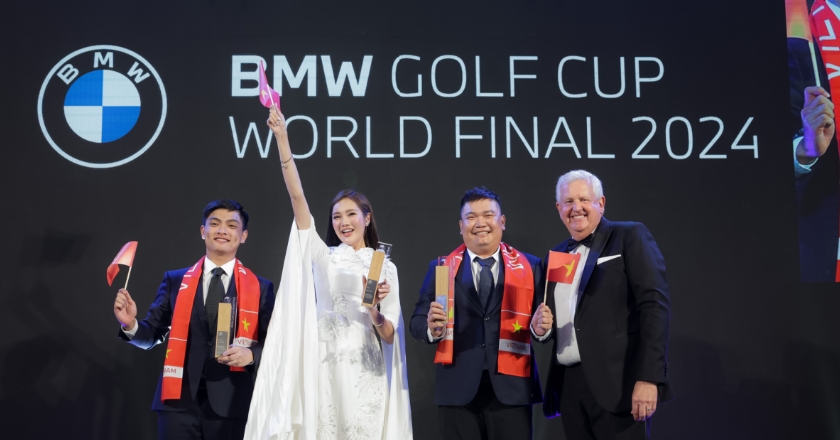 Vier Personen auf einer Bühne beim BMW Golf Cup World Final 2024 mit Pokalen und Landesflaggen vor einer Markenwand.