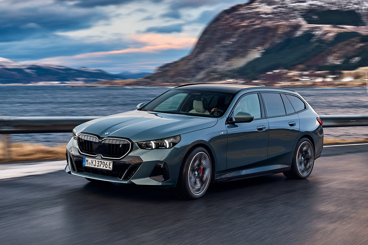 Grauer BMW i5 fährt autonom auf einer Straße am Meer entlang.