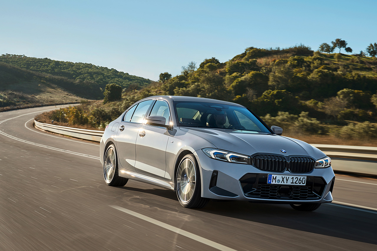Ein grauer 3er BMW fährt auf einer Straße durch eine schöne natürliche Landschaft.