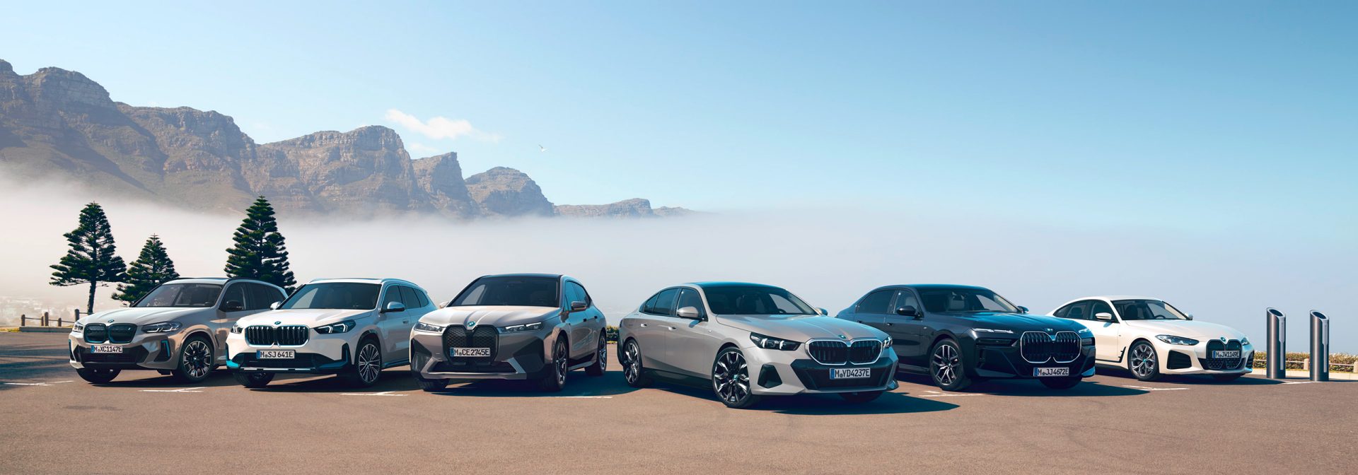 Sechs verschiedene BMW-Elektrofahrzeuge stehen vor einer Bergkulisse.