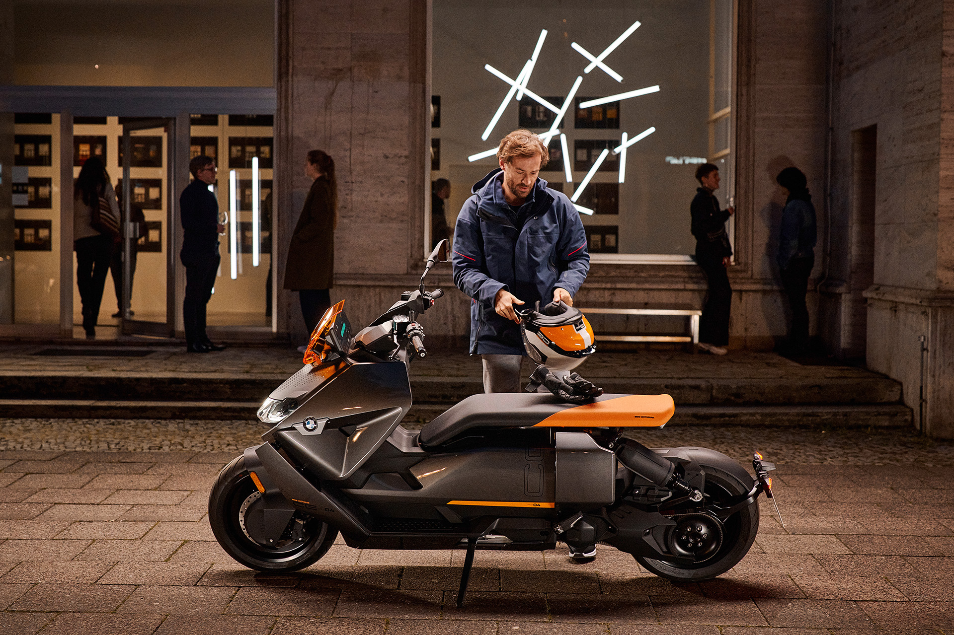 Ein junger Mann steht vor einem modernen Gebäude mit seinem BMW CE04 Roller.