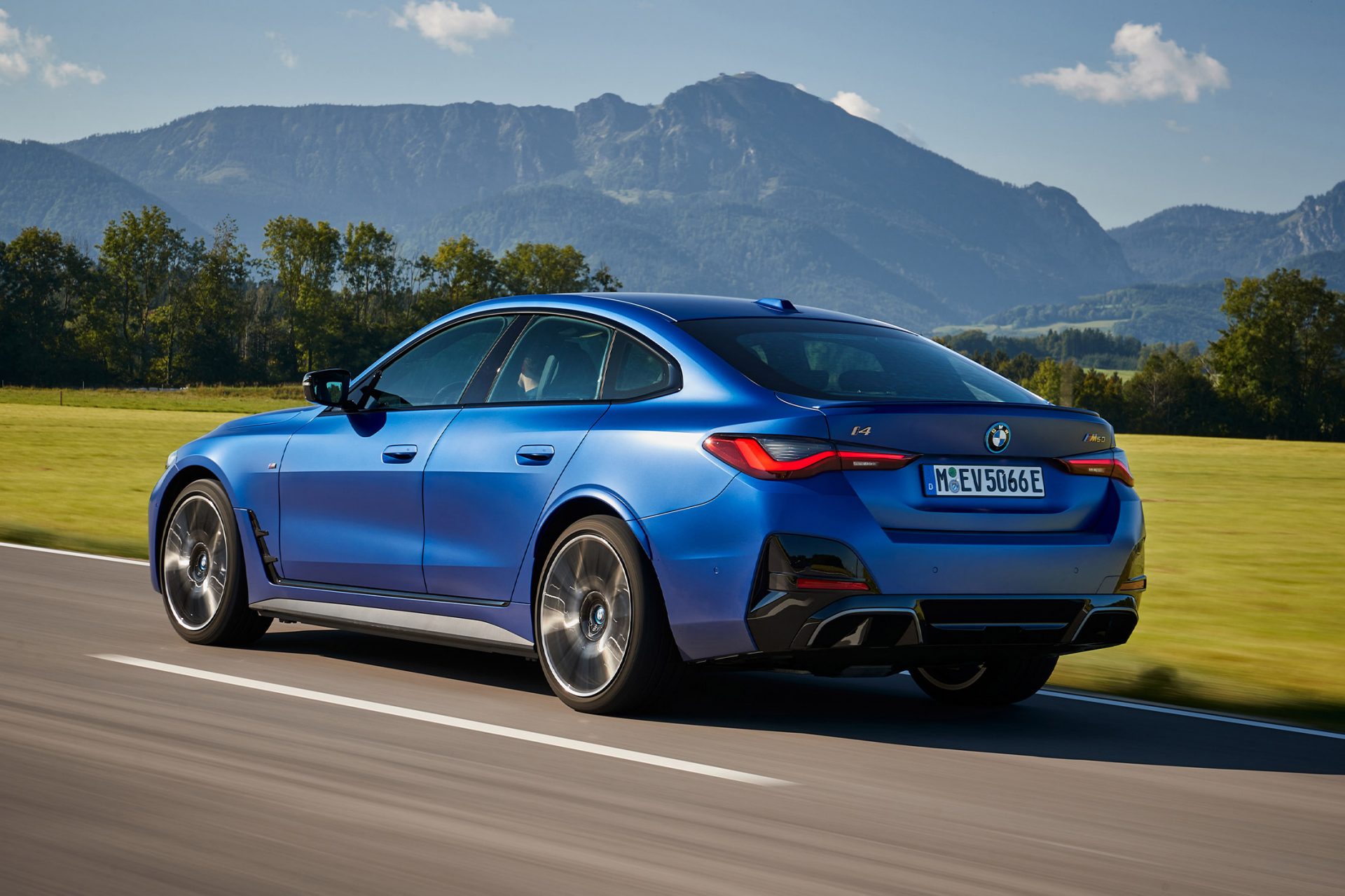 Ein blauer BMW i4 fährt auf einer Landstraße durch die Natur.