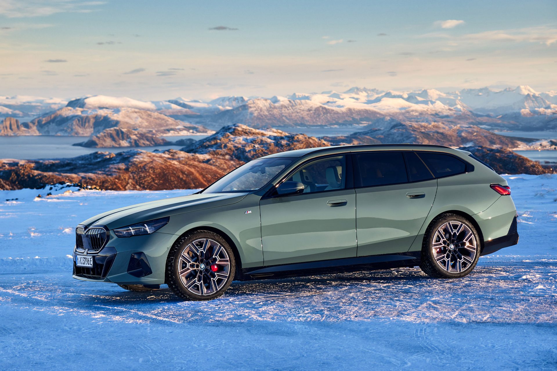 BMW i5 Touring geparkt im Schnee, im Hintergrund sind Berge zu sehen