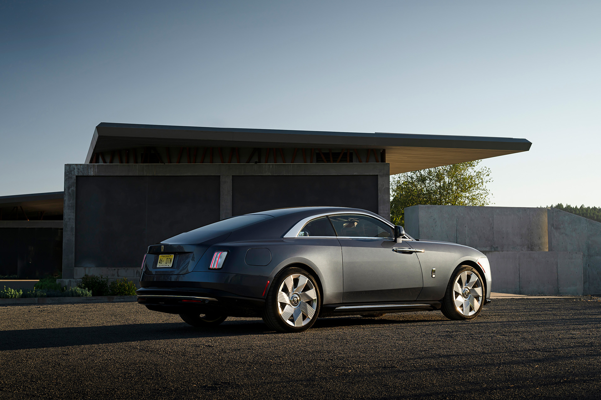 Ein grauer Rolls-Royce Spectre parkt neben einem futuristisch anmutenden Haus.