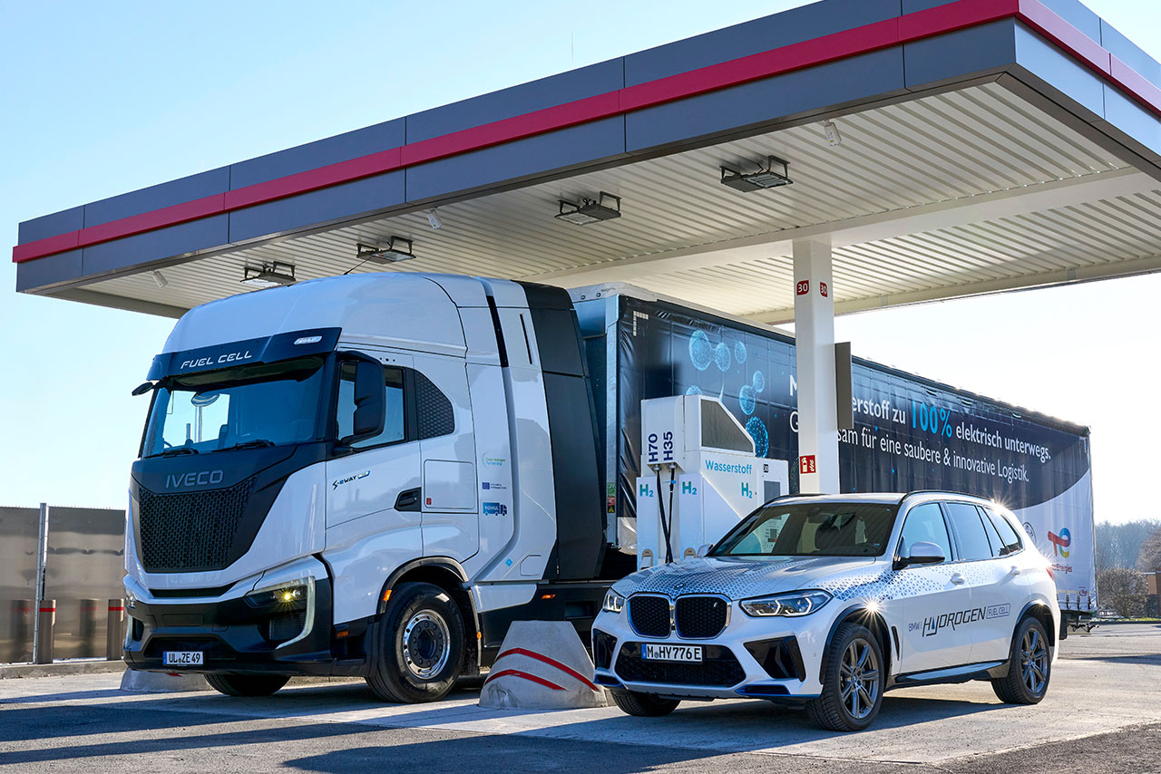 EIn BMW Wasserstoff Auto und ein IVECO Wasserstoff LKW an einer Tankstelle.