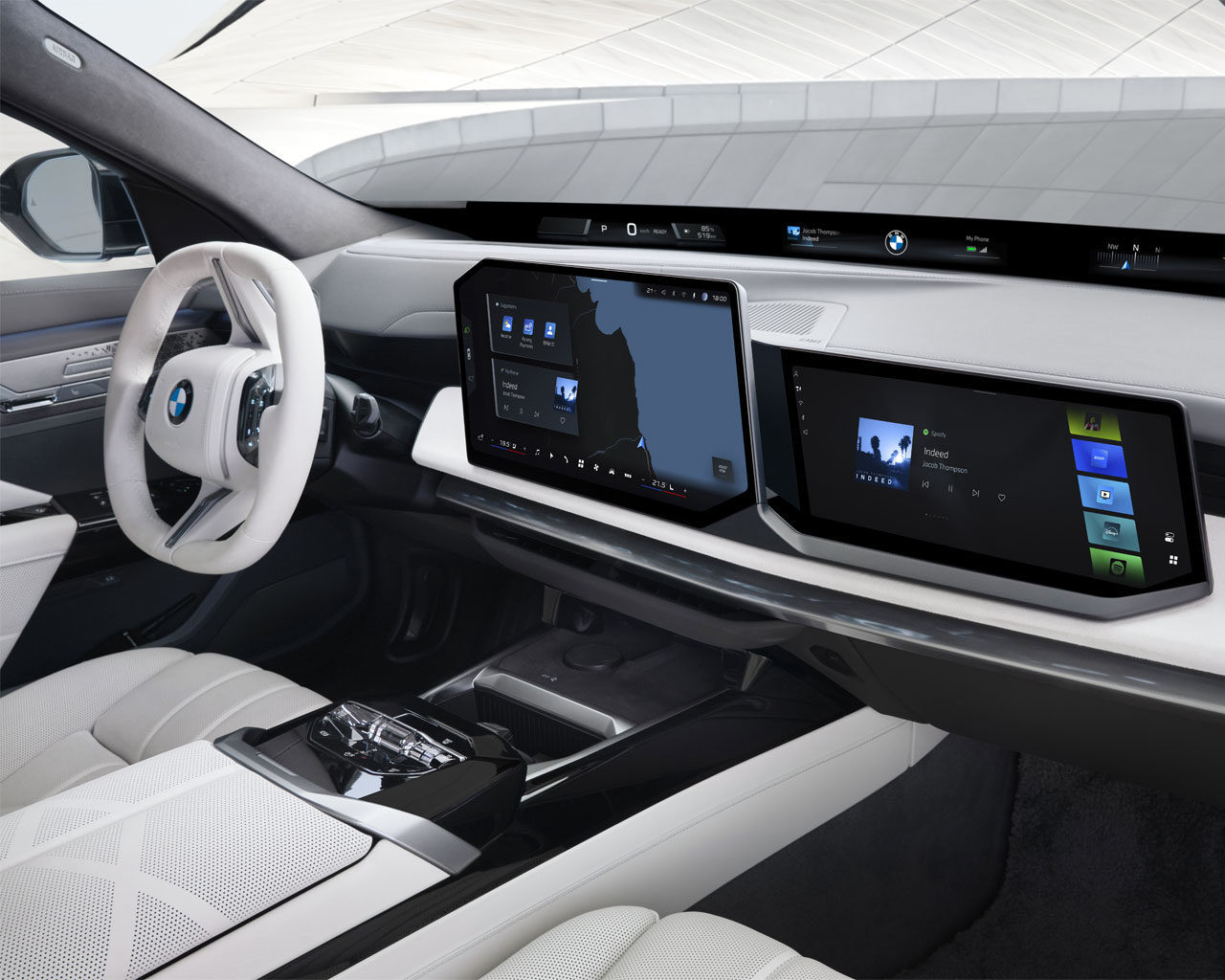 Blick ins Cockpit eines BMW 740 xDrive mit weißem Lenkrad: Das Zentraldisplay zeigt die Navigationskarte, das Beifahrer-Display Medienangebote und das BMW Panoramic Vision unter der Windschutzscheibe Fahrinformationen.