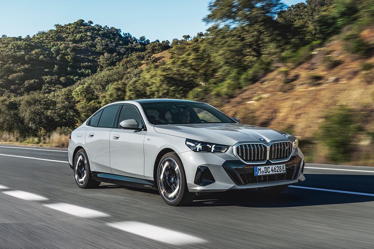 Grauer BMW i5 fährt auf einer Landstraße.