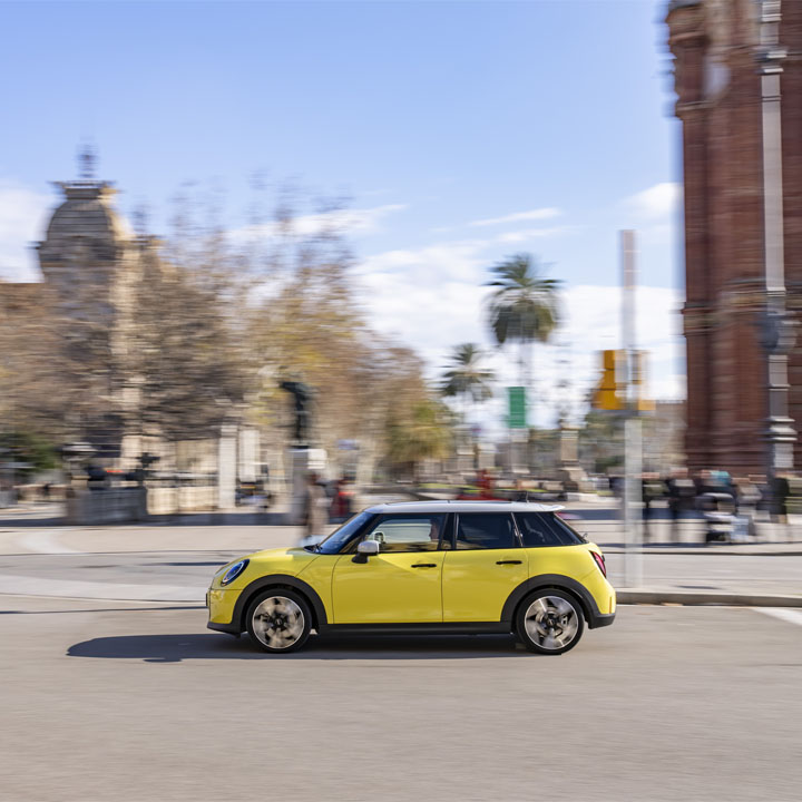 Ein gelber Mini Cooper bewegt sich durch eine belebte Stadtstraße.