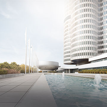 Rechts im Bild das BMW-Vierzylinderhochhaus, links Fahnenmasten und ein Wasserbecken auf einer gepflasterten Fläche.