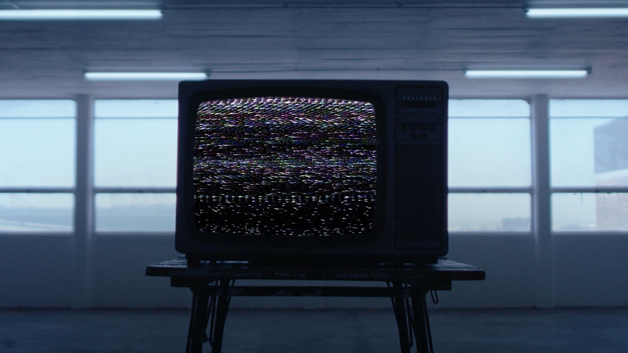 Fernseher mit rauschendem Bild auf einem Hocker in einem leeren Raum.