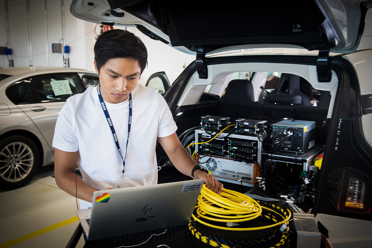 Ein Mann arbeitet an seinem Laptop, während er neben einem geparkten Auto steht.
