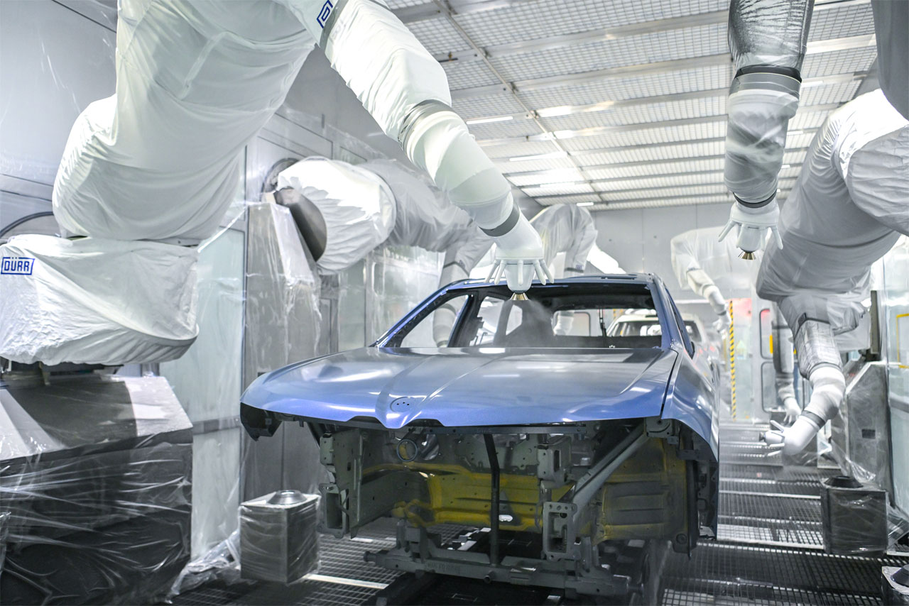 Blaue Karosserie eines BMW iX3 in der Lackiererei des BMW Group Werk in Debrecen, Roboter sprühen Lack auf die Fronthaube.