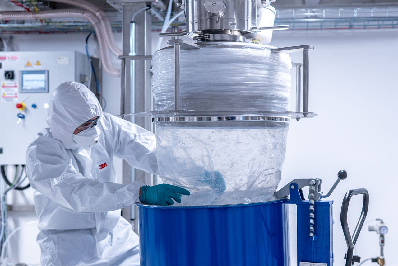 Im BMW Group Kompetenzzentrum Batteriezellrecycling (CRCC) entleert eine Fachkraft im weißen Schutzanzug über eine Edelstahlvorrichtung recyceltes Batteriematerial in einen blauen Container.