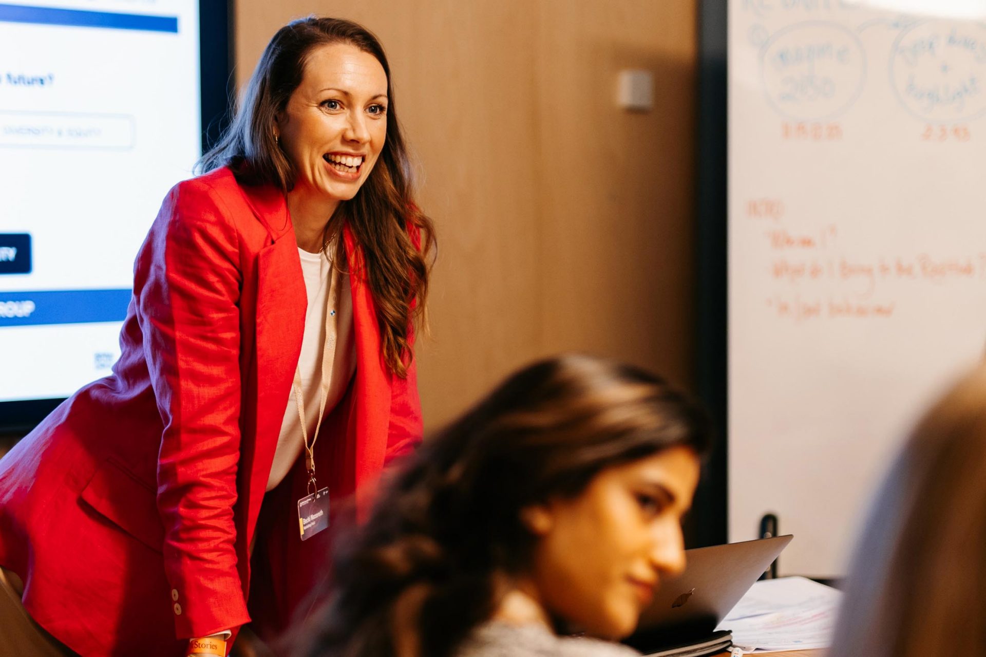  Eine Frau in einem roten Blazer leitet ein Teammeeting.