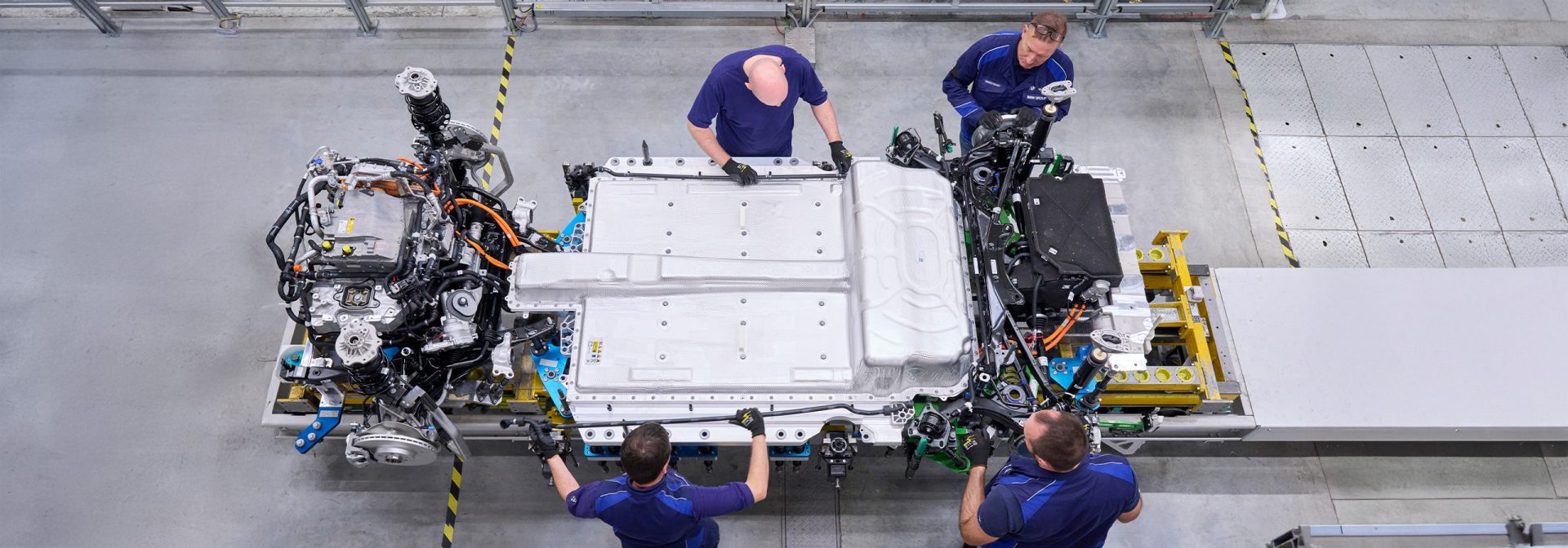 Vier Personen arbeiten an einer großen technischen Anlage mit Kabeln und Metallteilen in einer hellen Werkstatt.