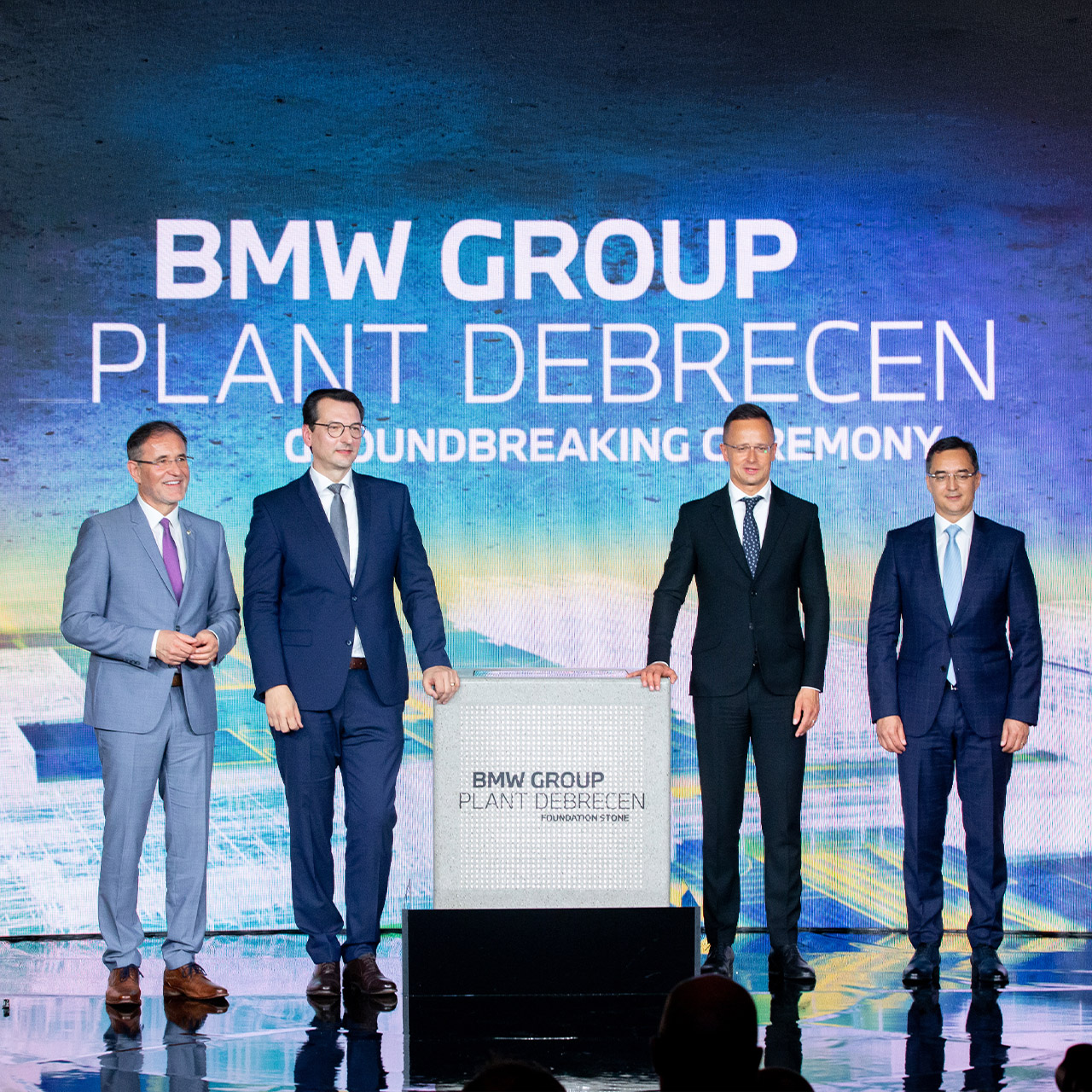Vier Herren aus dem Vorstand der BMW Group auf einer Bühne, im Hintergrund steht BMW Group Plant Debrecen auf einer großen Leinwand.
