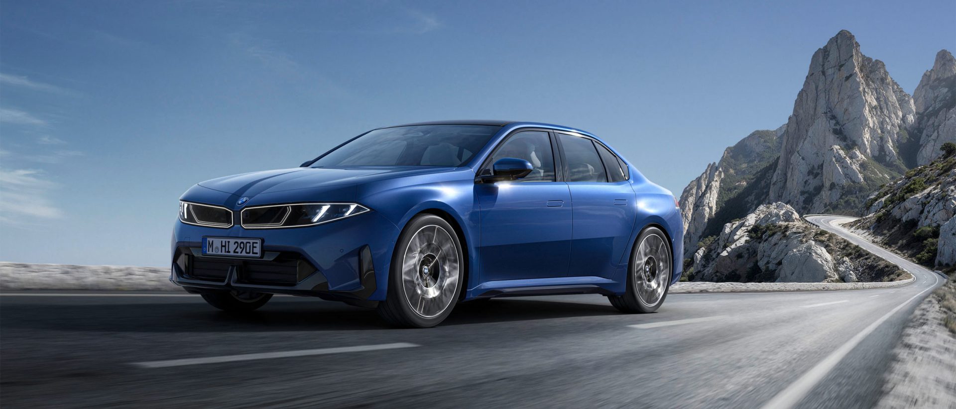 Blue BMW i3 Neue Klasse on a winding mountain road with rocky landscape in the background.