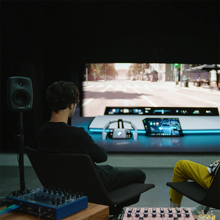 Two BMW Group sound designers in their studio, surrounded by tech, look at a virtual front screen with BMW Panoramic iDrive.