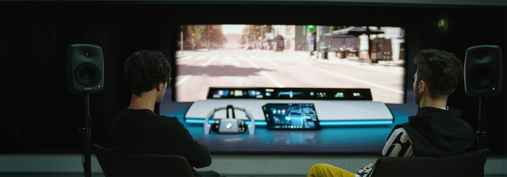 Two BMW Group sound designers in their studio, surrounded by tech, look at a virtual front screen with BMW Panoramic iDrive.