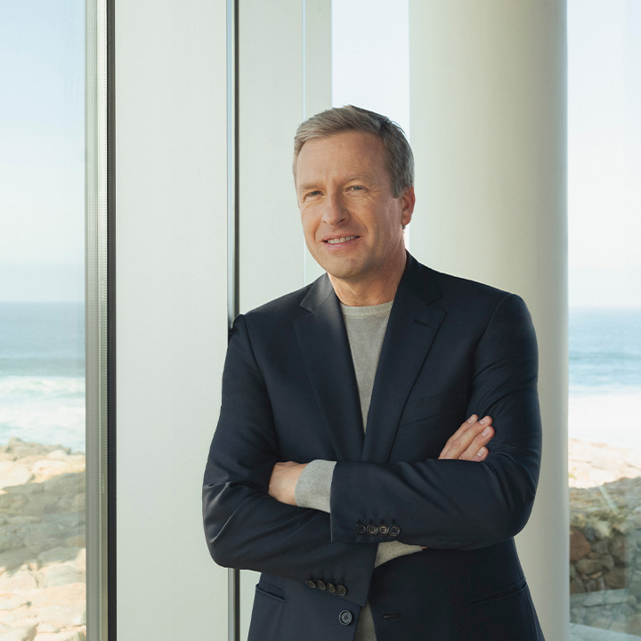 Oliver Zipse the CEO of the BMW Group standing next to a windowfront. The Sea in the background.