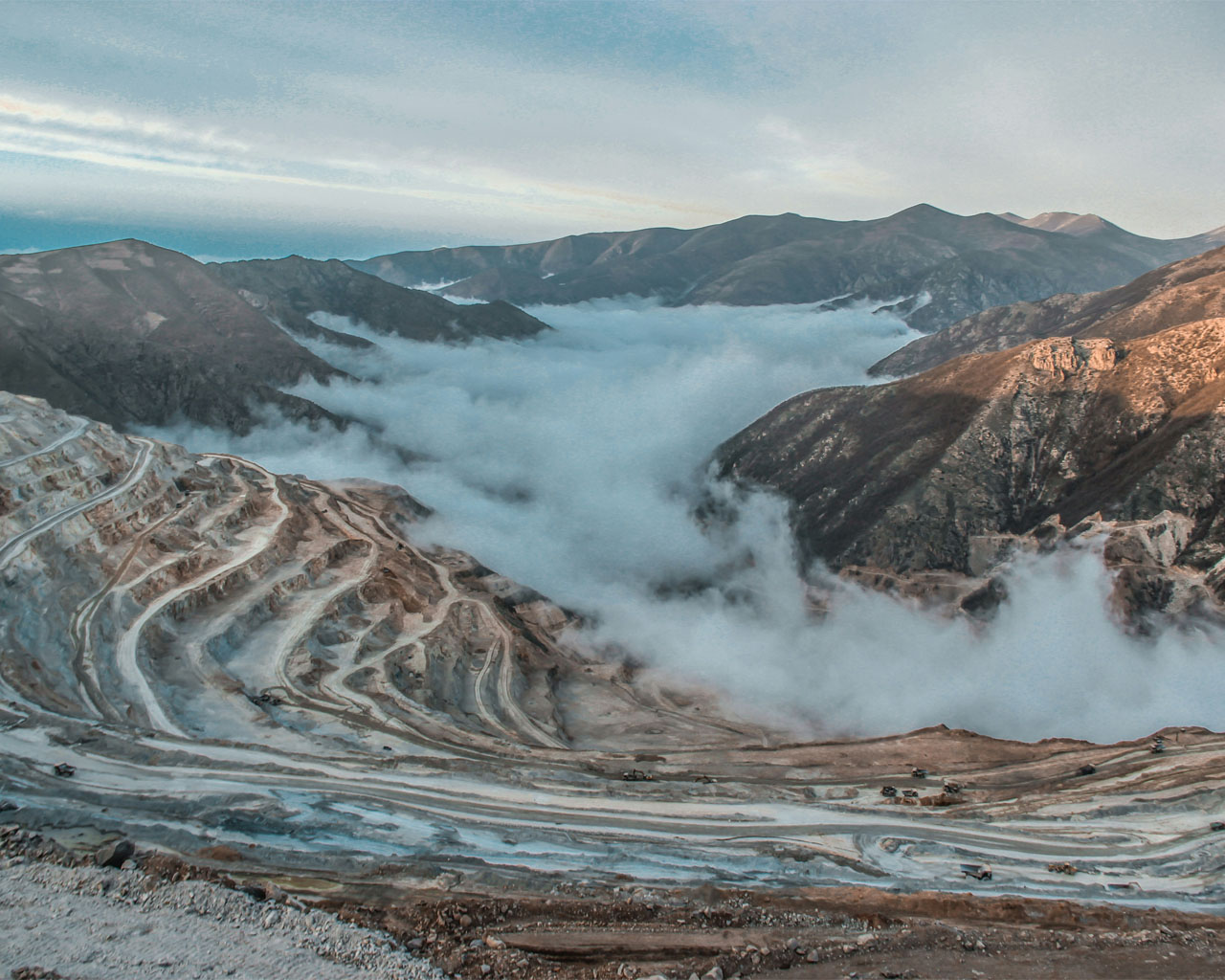 White snow covers the mountains as clouds gently drift overhead, shrouding the landscape.