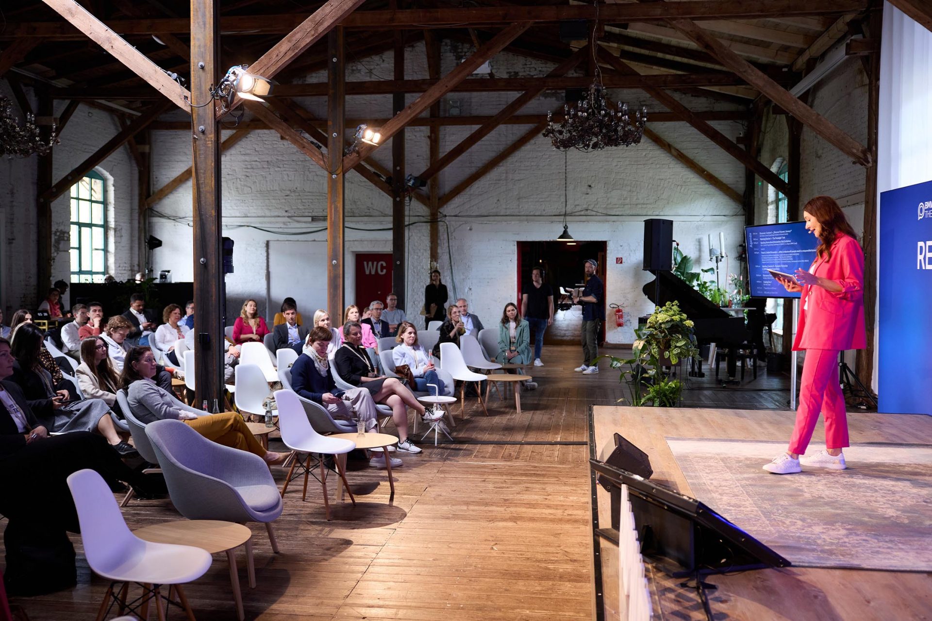   A young woman in a pink suit is giving a presentation on stage