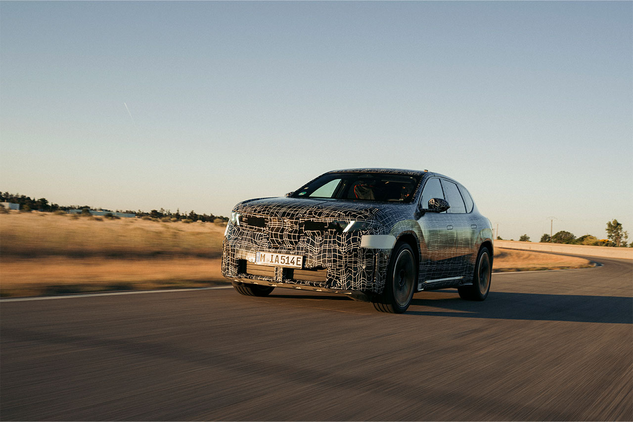 The prototype of the BMW iX3 50 xDrive drives on a country road.