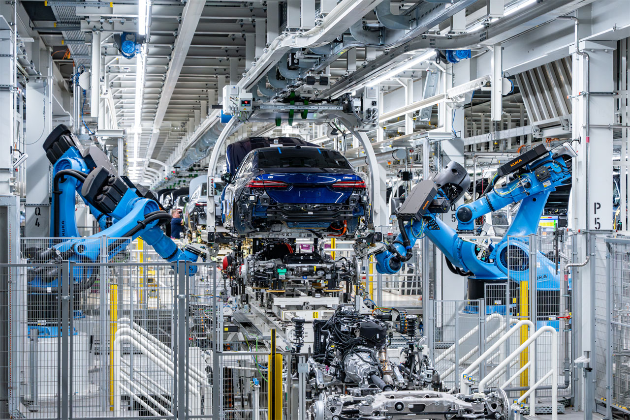 Factory hall with two large industrial robots working on the rear of a blue car.