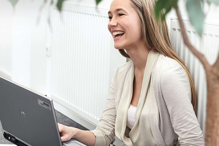 A female apprentice sits on the floor with her computer and laughes.