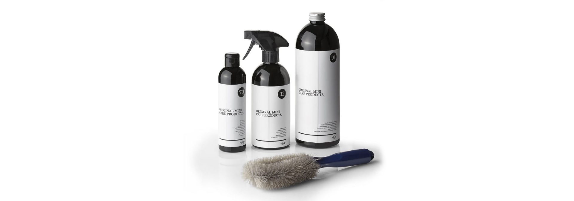 Three differently sized bottles labeled 'ORIGINAL MINI CARE PRODUCTS' and a brush with a blue handle and gray bristles on a white background.