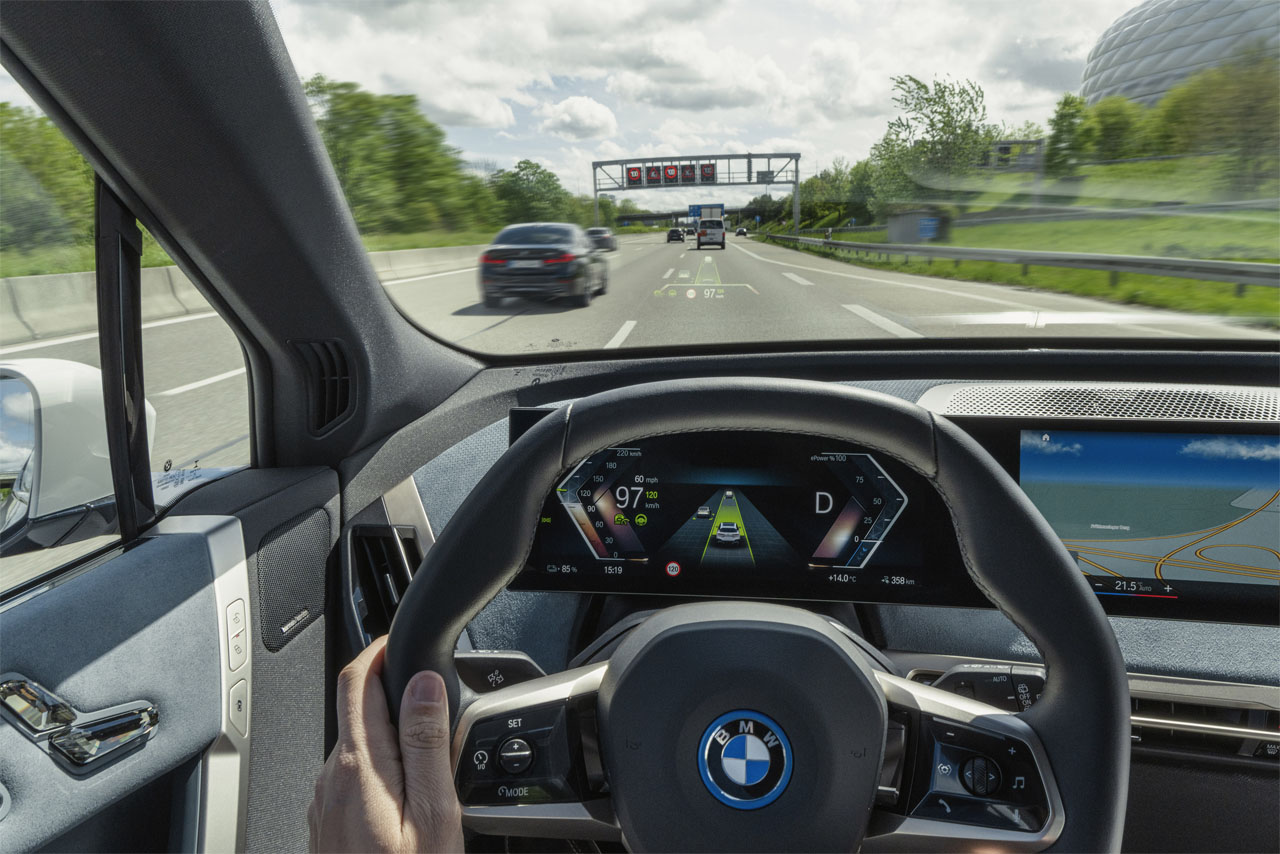 View from the driver's seat of a BMW onto the steering wheel and the digital dashboard with navigation display on a highway.