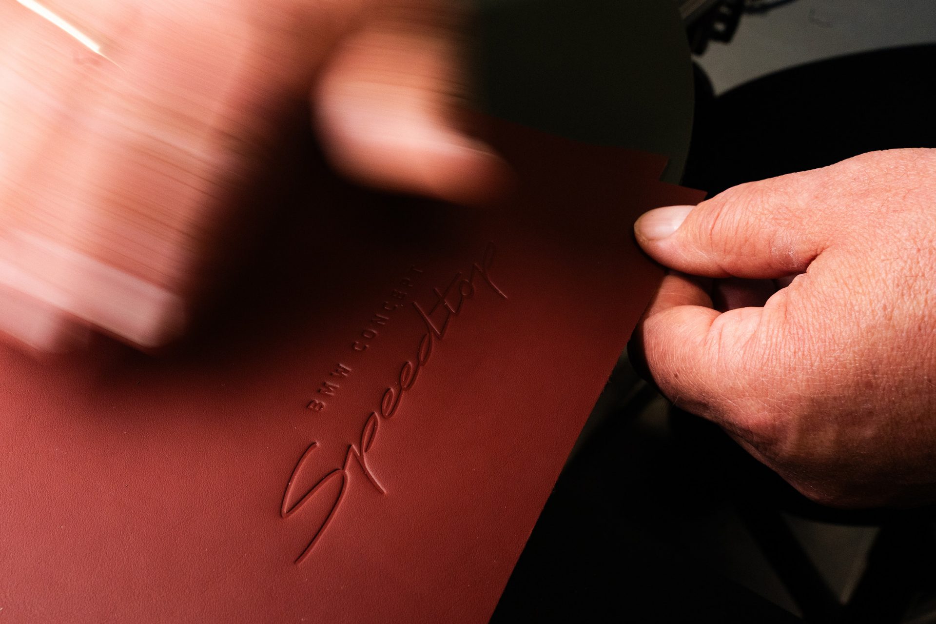 A saddler is working on a red piece of leather with the inscription BMW Concept Speedtop.