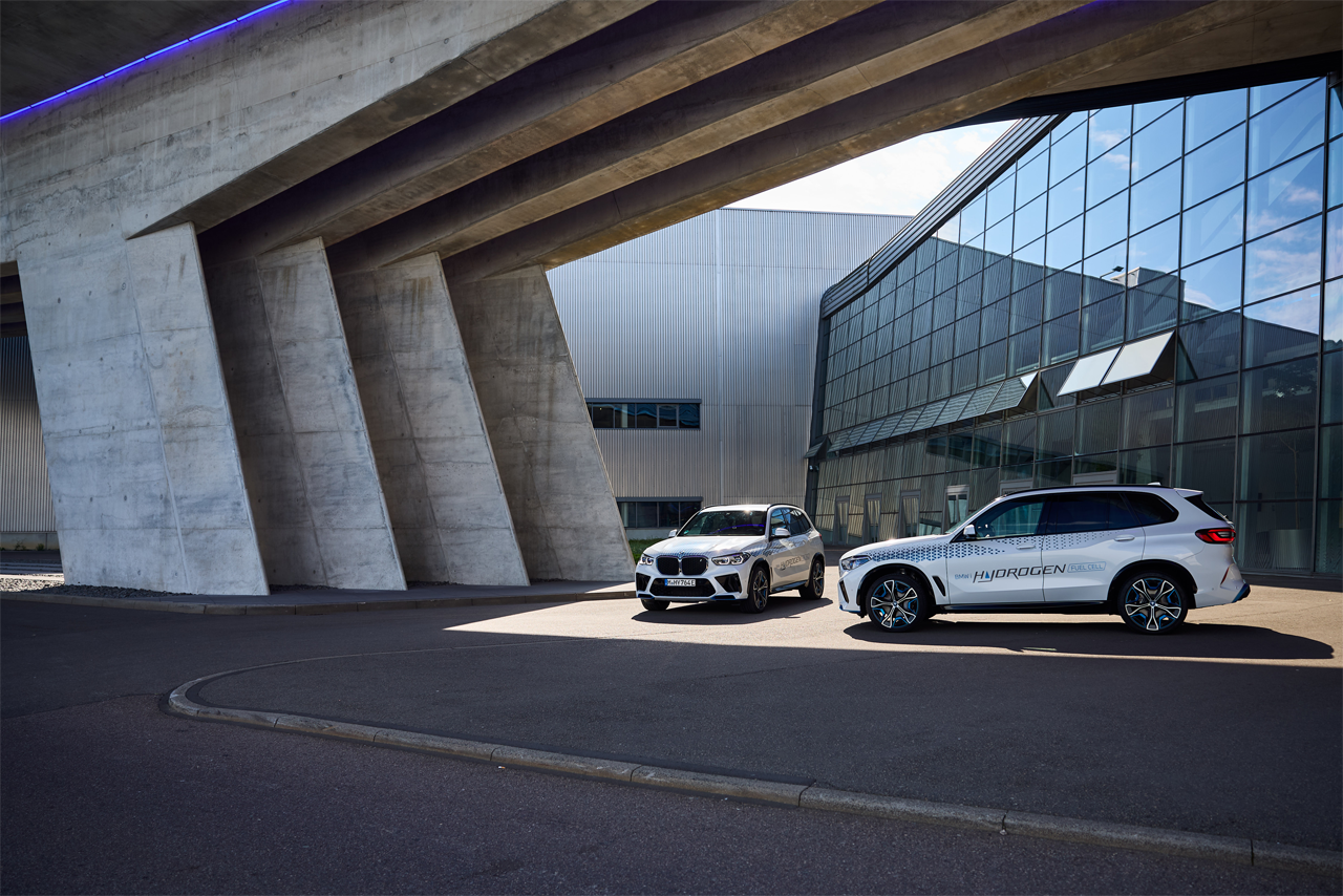 Two hydrogen-powered BMW vehicles parked infront of a modern production hall.