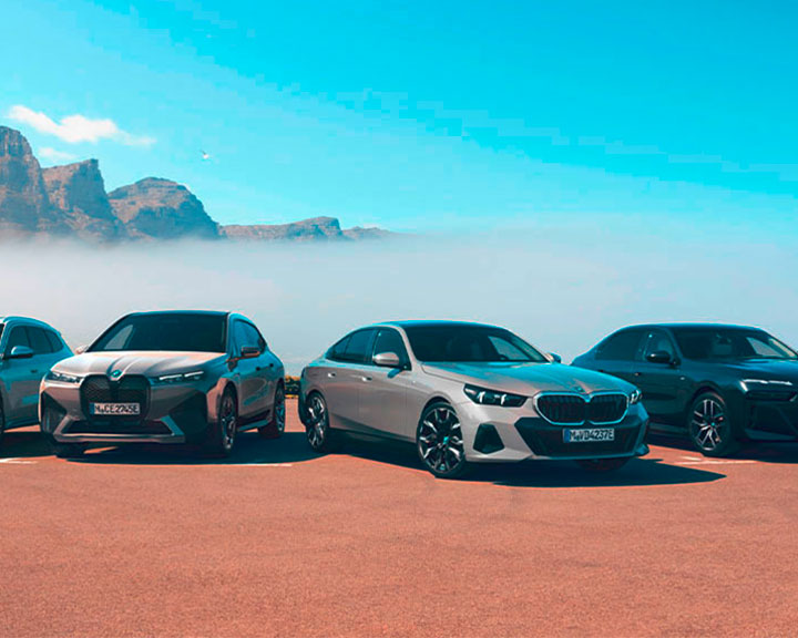 Three different electric cars, a BMW iX, a BMW i5 and a i7 are parked infront of the mountains.