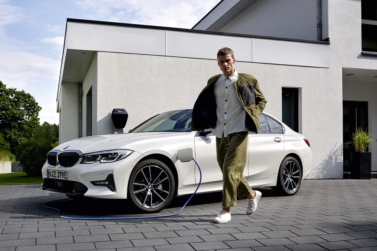 A man charging a white BMW 3 series onfront of his house