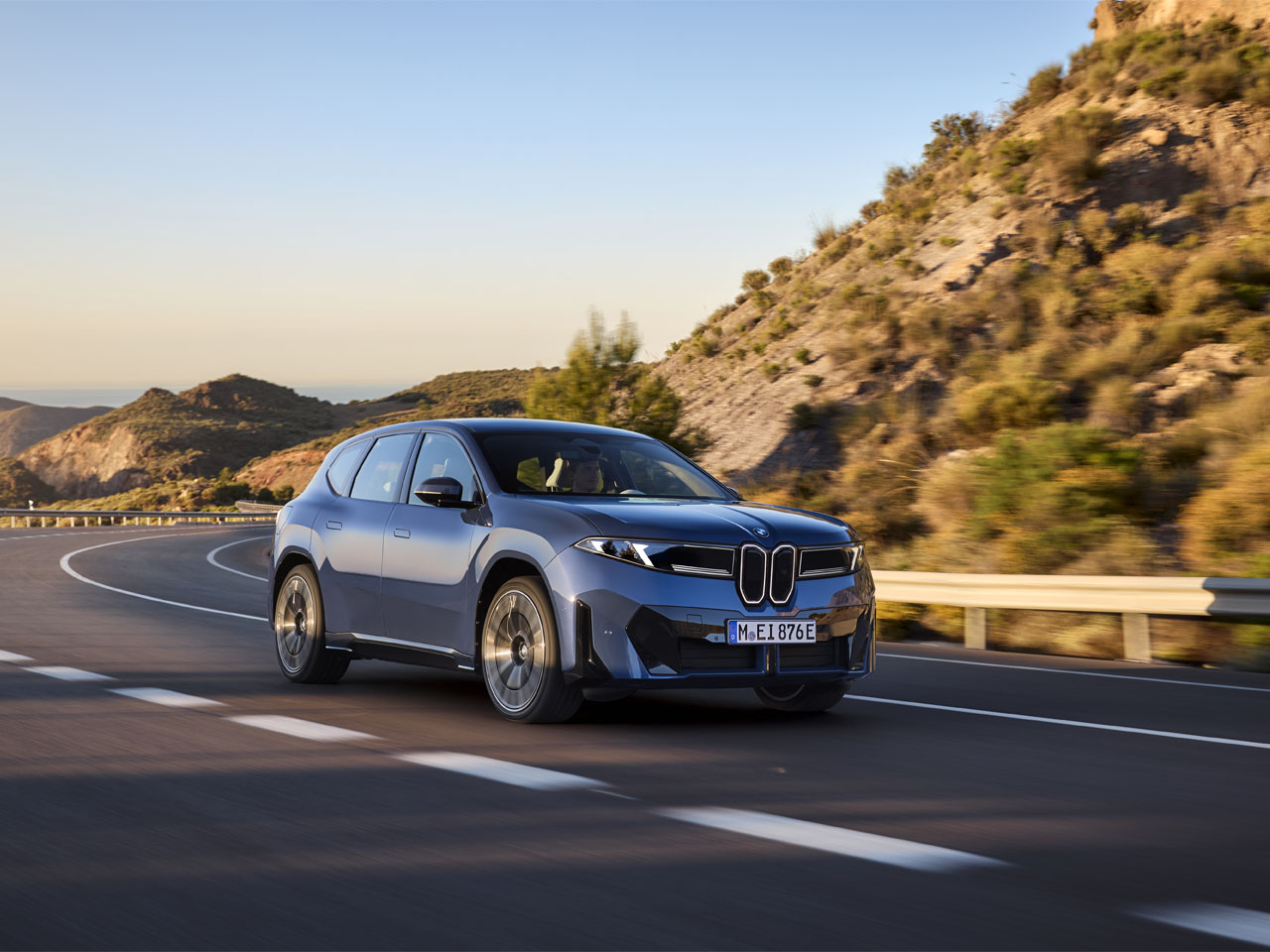 A blue BMW iX3 driving on a scenic road along the sea.