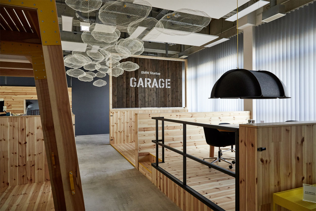 Modern office space with wooden paneling, a round table, and black chairs. BMW Startup Garage is displayed on the wall in the background.