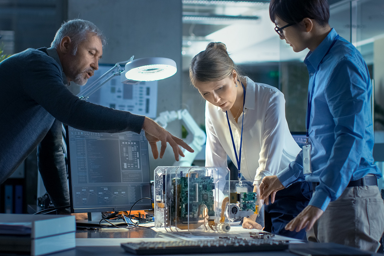 Team of Computer Engineers Lean on the Desk and Choose Printed Circuit Boards to Work with.