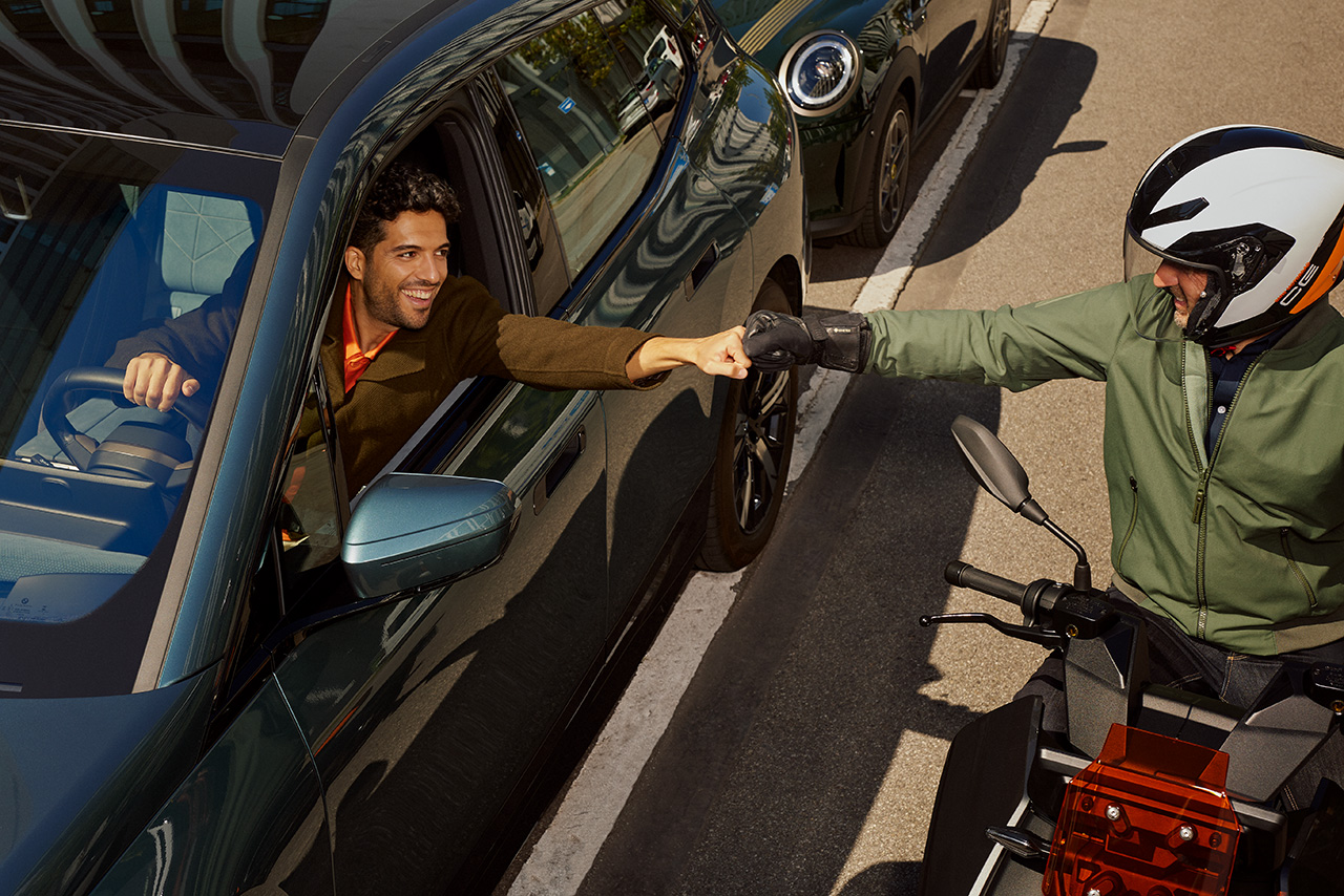 A driver and a motorcyclist are fist bumping on the road